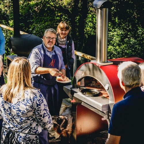 Pizza chef teaching students how to use a wood fired pizza oven outside