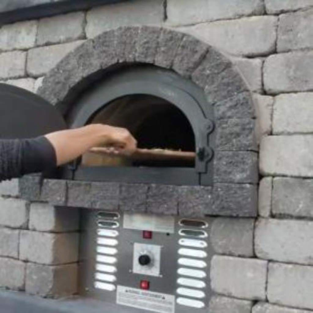 Chicago Brick Oven CBO 750 Hybrid Gas and Wood Fired Pizza Oven DIY Kit Custom Stone Back Patio Home Installation with Door Open and Cooking Pizza