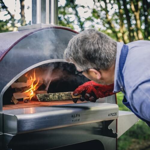 Man putting wood inside a pizza oven with fire