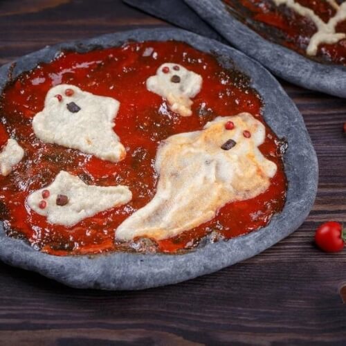 Black charcoal crust halloween pizza with ghosts on top in red sauce