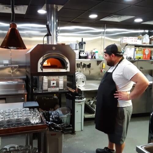 Man looking inside his hybrid pizza oven