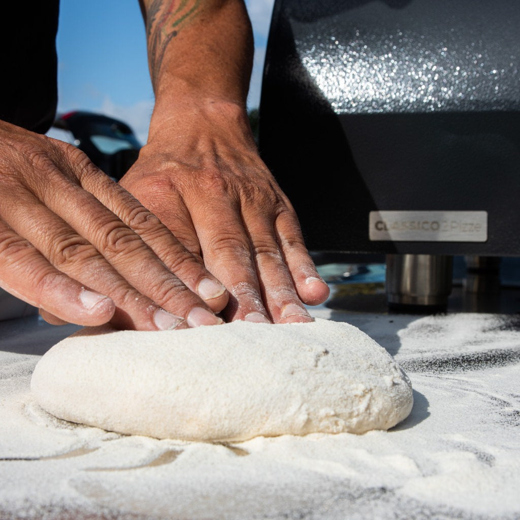 ALFA Classico 2 Pizza Gas oven in background while man is kneading pizza dough by hand on a prep table outside