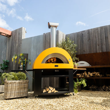 Alfa Allegro Pizza Oven Base with yellow outdoor pizza oven on top with wood storage in a backyard setting