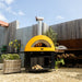 Alfa Allegro Pizza Oven Base with yellow outdoor pizza oven on top with wood storage in a backyard setting