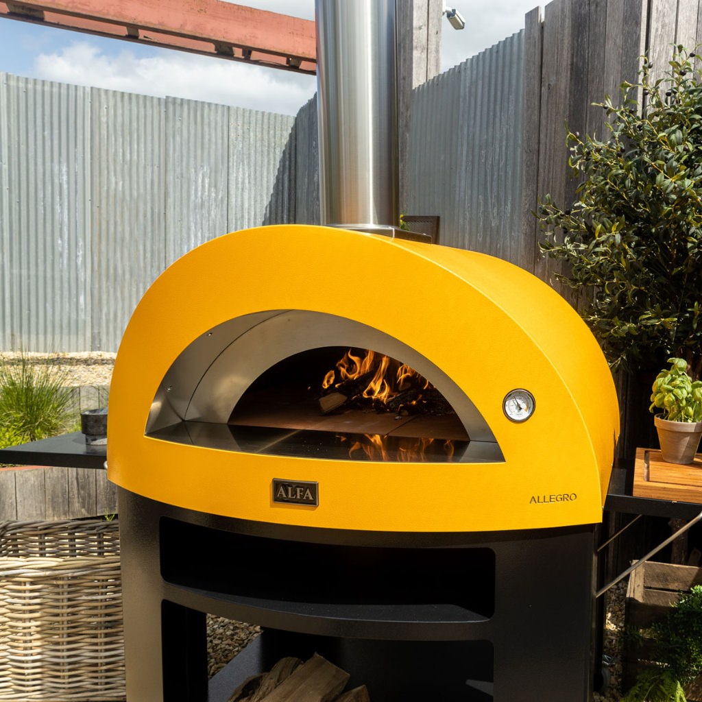 Alfa Allegro Pizza Oven Base with yellow outdoor pizza oven with flames inside in a backyard setting.