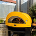 Alfa Allegro Pizza Oven Base with yellow outdoor pizza oven with flames inside in a backyard setting.