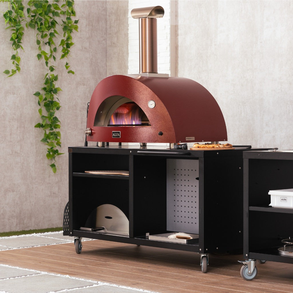 Alfa Forni Cooking Station 160 in outdoor kitchen with red modern stainless steel pizza oven on the cooking station with a wooden floor and cement wall in the background.