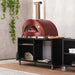 Alfa Forni Cooking Station 160 in outdoor kitchen with red modern stainless steel pizza oven on the cooking station with a wooden floor and cement wall in the background.