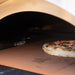Alfa Kit Hybrid burner cover inside wood-fired oven with a pizza baking on the cooking floor
