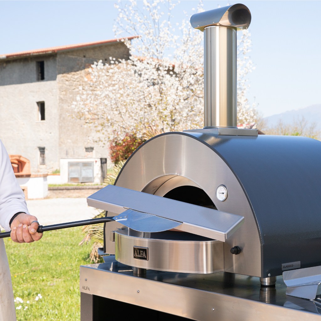 Alfa Kit Hybrid with man putting gas cover inside a gas pizza oven outdoors with a scenic Italian background