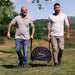 Alfa Moderno Portable Cover with two men walking in a grassy outdoor setting each holding one handle of the cover