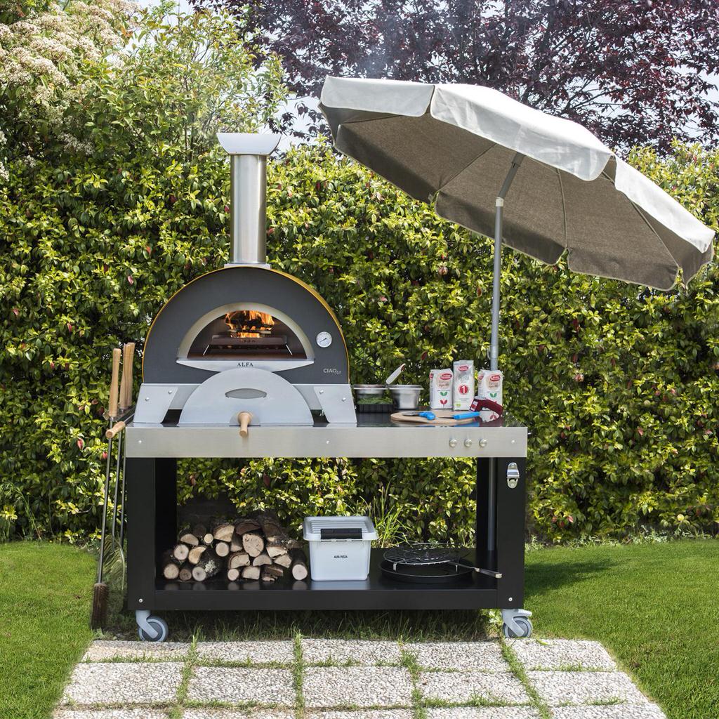 Alfa Pizza Table with outdoor pizza oven on top with an umbrella in a garden setting