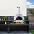 Amazing outdoor kitchen with an Alfa 5 Minuti wood fired pizza oven with a fire burning inside it sitting on a black stone countertop with wood beneath it