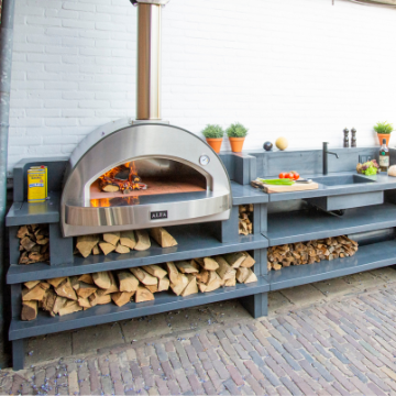 Beautiful outdoor kitchen with an Alfa 4 Pizze wood fired pizza oven burning wood inside it while sitting on a custom made concrete countertop