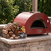 Red Alfa outdoor pizza oven with split oak firewood and Qwick Wick fire starters on a stone outdoor kitchen counter.