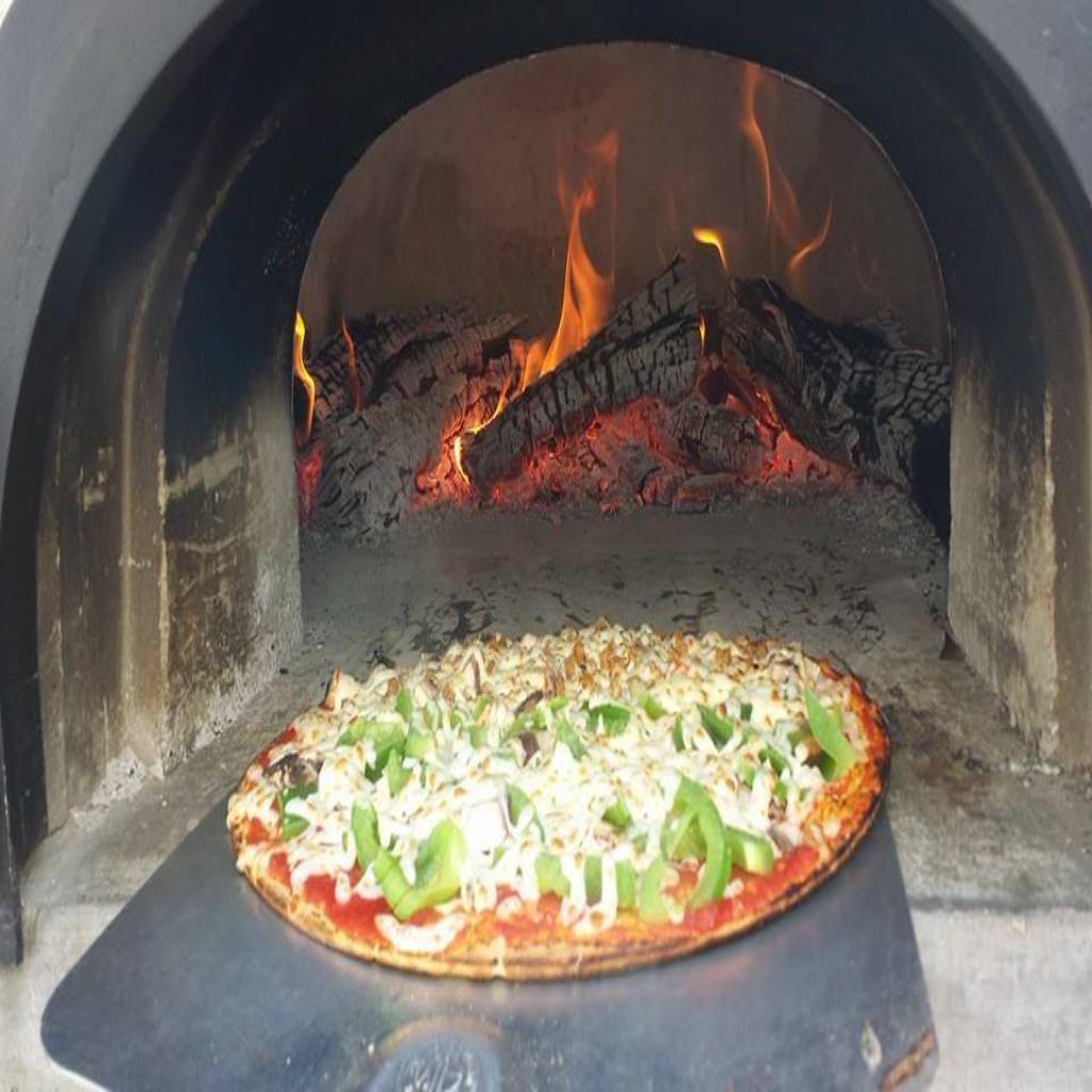 Chicago Brick Oven CBO 1000 Commercial Wood Fired Pizza Oven Kit Cooking Pizza on Pizza Peel with Wood Burning in the Background