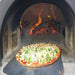 Chicago Brick Oven CBO 1000 Commercial Wood Fired Pizza Oven Kit Cooking Pizza on Pizza Peel with Wood Burning in the Background