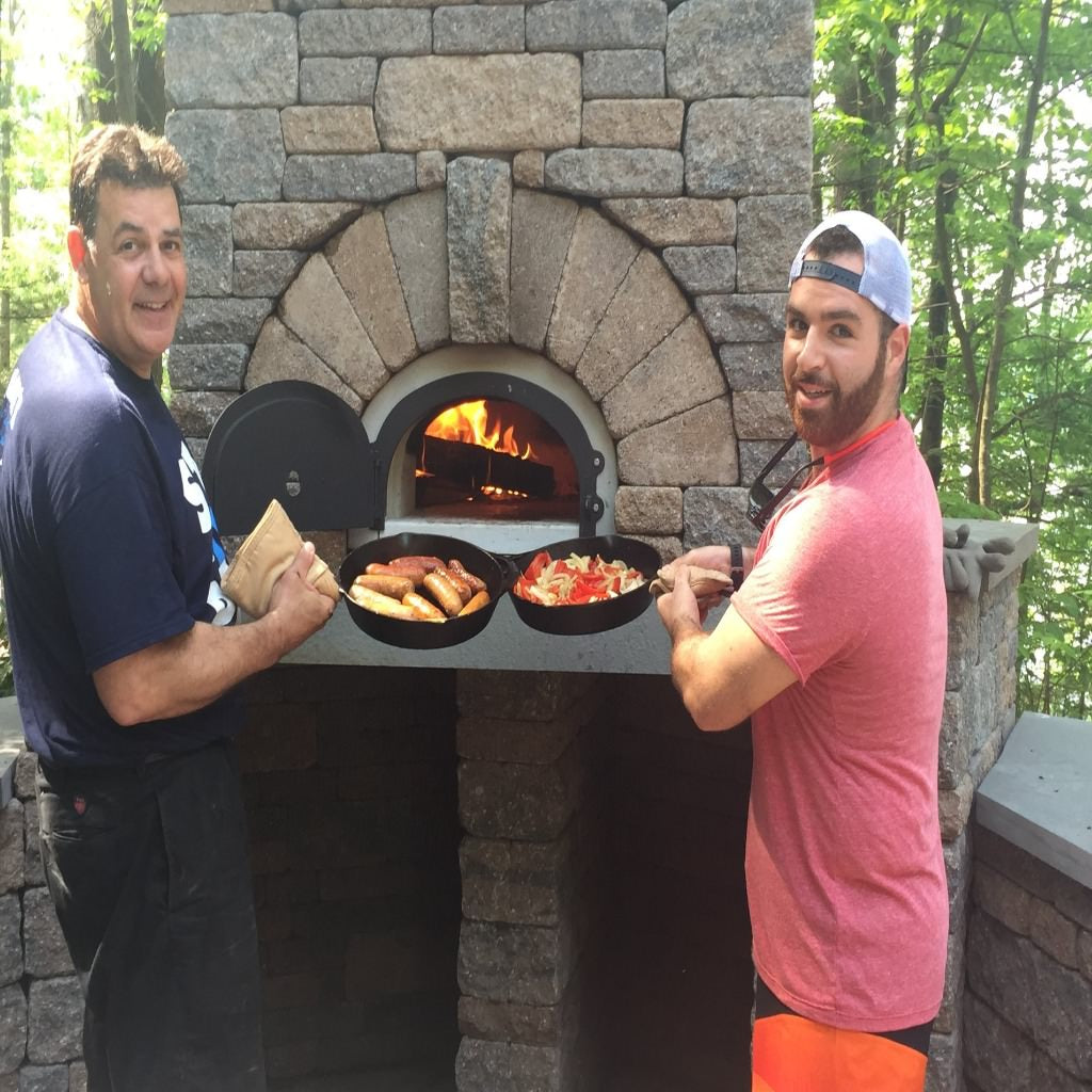 Chicago Brick Oven CBO 1000 Commercial Wood Fired Pizza Oven Kit Cooking Bratwursts and Vegetables with Father and Son