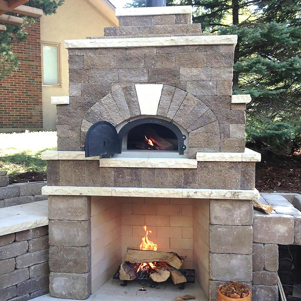 Chicago Brick Oven CBO 1000 Commercial Wood Fired Pizza Oven Kit Custom Stone Patio Installation with Fireplace Below Oven and Fire Burning in Both