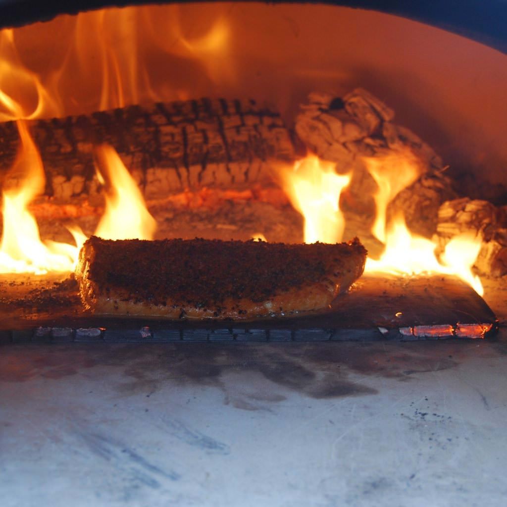 Chicago Brick Oven CBO 500 Countertop Wood Fired Pizza Oven Cooking Fish with Fire Burning in the Background of the Oven