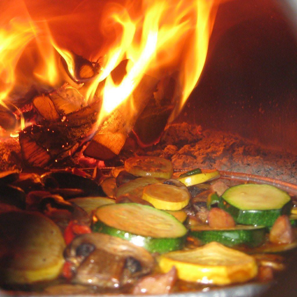 Chicago Brick Oven CBO 500 Countertop Wood Fired Pizza Oven Cooking Vegetables with Fire Burning in the Background of the Oven