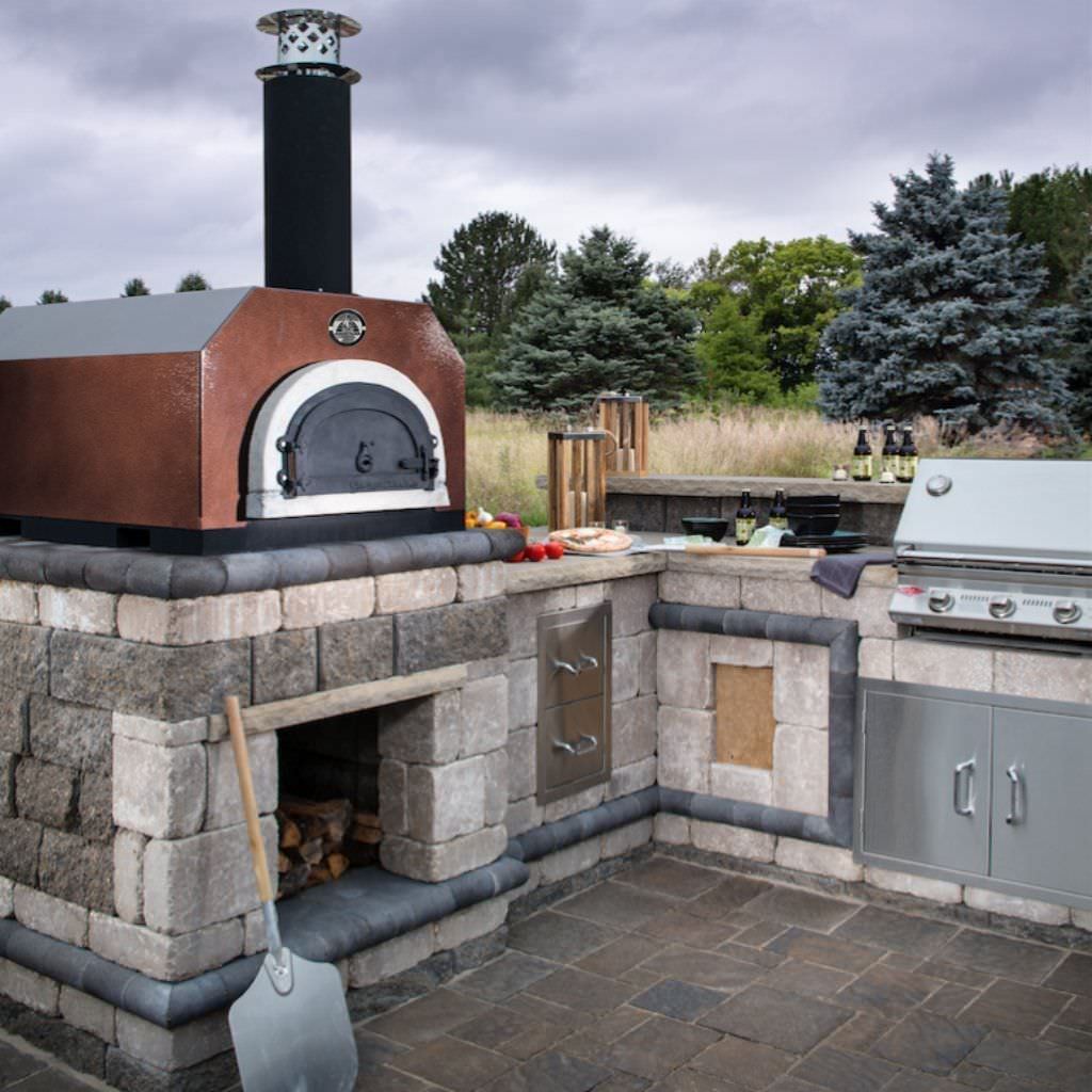 Chicago Brick Oven CBO 750 Countertop Wood Fired Pizza Oven in Copper Vein in Custom Built Outdoor Kitchen with Grill and Trees in the Background