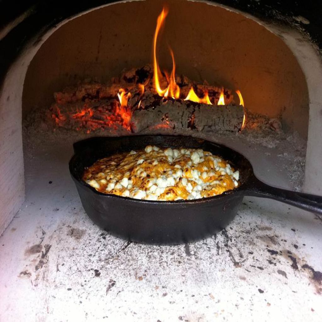 Chicago Brick Oven CBO 750 Hybrid Countertop Gas and Wood Fired Pizza Oven Cooking in Cast Iron Pan with Fire Burning in the Oven