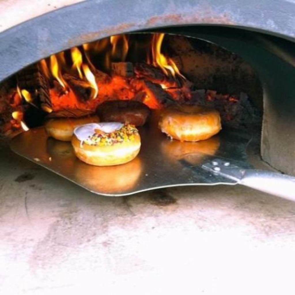 Chicago Brick Oven CBO 750 Commercial Wood Fired Pizza Oven Trailer Cooking Donuts with Fire Burning in the Background of the Oven