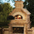 Chicago Brick Oven CBO 750 Wood Fired Pizza Oven DIY Kit Custom Backyard Stone Installation with Oven Door Open and Fire Burning in Summer