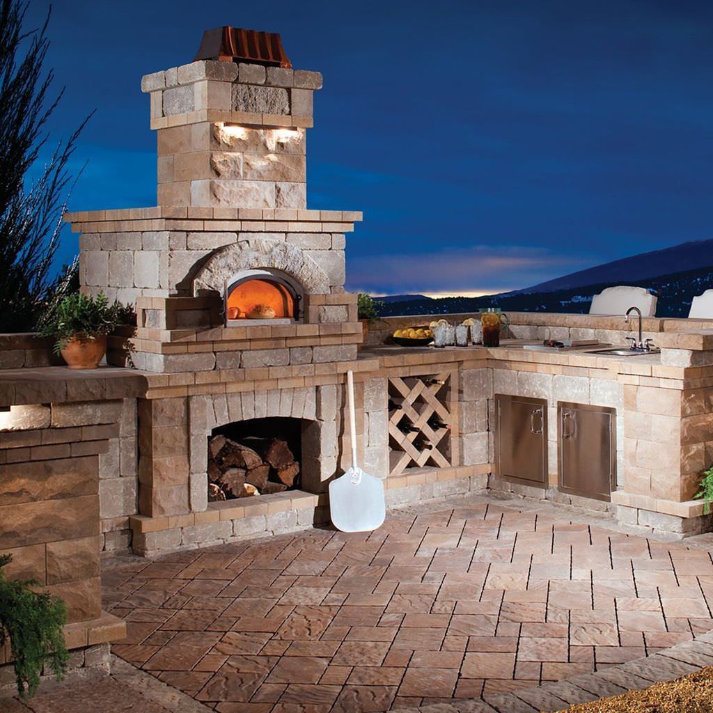 Chicago Brick Oven CBO 750 Wood Fired Pizza Oven DIY Kit in Custom Stone Outdoor Kitchen with Fireplace and Sink at Night