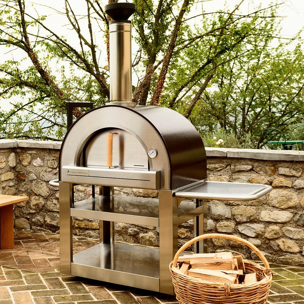 Forno Venetiza Pronto 500 outdoor pizza oven on stone patio with a basket of wood next to it.